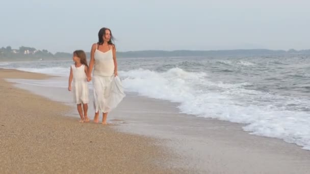 日落时 妈妈和女儿一起在海滩上散步 它们沿着大海的边缘行走 与水一起飞溅 — 图库视频影像
