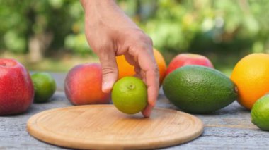 Olgun kireç kesme tahtasında doğranır. Masada taze meyveler var. İkiye bölünmüş limon suyu. Arka planda Avokado Limonu ve Elma.