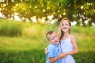 Tatlı çocuklar akşam parkında yürüyorlar. Sarıl ve gülümse. Çocuklar rahatlar ve dışarıda oynarlar. Çocukluk.
