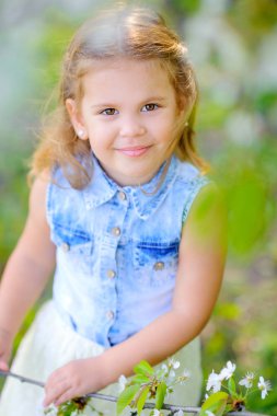 Bir bahar parkında çiçekli bir ağacın yanında elbise giymiş tatlı bir kız. Çocuklar rahatlar ve dışarıda oynarlar. Çocukluk.