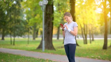 Sporcu şafakta parkta antrenman yapıyor. Sporcu pist boyunca koşar, kulaklıkla müzik seçer ve dinler. Sağlıklı yaşam tarzı.