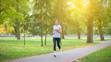 Sporcu şafakta parkta antrenman yapıyor. Sporcu pist boyunca koşar, kulaklıkla müzik dinler. Sağlıklı yaşam tarzı.