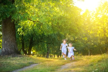 Gün batımında sevimli çocuklar parkta yürüyor. Kızlar yol boyunca koşar ve eğlenir. Çocuklar dışarıda oynayıp eğleniyorlar..