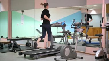 Spor salonunda koşu bandında koşan güzel bir kadın. Fitness ve sağlıklı yaşam tarzı konsepti. Sporcu kadın fitness merkezinde çalıştırma makinesi kullanıyor.
