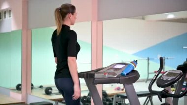 Güzel bir kız spor için spor salonunda koşu bandında yürür. Fitness ve sağlıklı yaşam tarzı konsepti. Sporcu kadın fitness merkezinde çalıştırma makinesi kullanıyor.