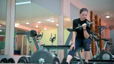 Spor salonunda ağırlık çalışmasıyla kol egzersizi yapan genç bir bayan sporcu. Fitness kızı aktif. Sağlık hizmetleri. Spor konsepti.