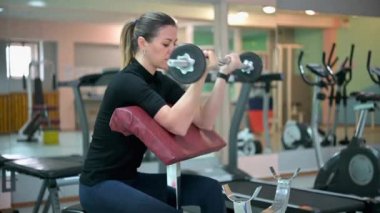 Spor salonunda ağırlık çalışmasıyla kol egzersizi yapan genç bir bayan sporcu. Sağlık Hizmetleri Spor Konsepti.