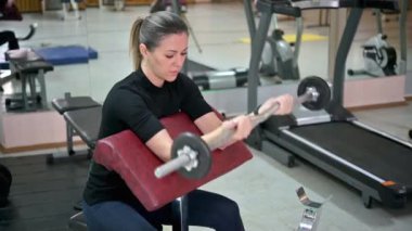 Spor salonunda ağırlık çalışmasıyla kol egzersizi yapan genç bir bayan sporcu. Fitness kızı aktif. Sağlık hizmetleri. Spor konsepti.