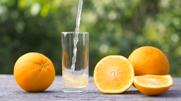 庭の木のテーブルの上に新鮮なオレンジジュースをグラスに注ぐ 健康食品のコンセプト — ストック動画