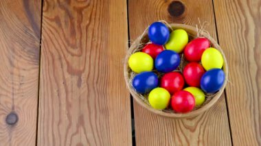 Renkli paskalya yumurtaları, ahşap bir masada, bir sepetin içindeki yumurta sarısı üzerinde yatar. Paskalya süsleri. Paskalya konsepti arka planı.