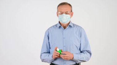 Tıbbi maskeli yaşlı bir adam beyaz bir arka planda izole edilmiş antibakteriyel spreyle ellerini tedavi ediyor. Sağlık ve tıbbi konsept. virüs koruması