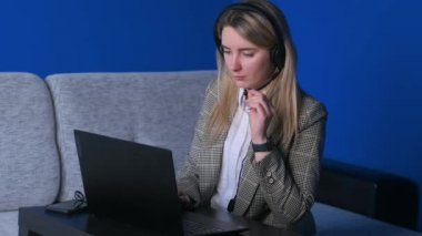 Genç serbest çalışan kız konferans görüşmesiyle iletişim kuran kulaklık takıyor ev ofisindeki bilgisayara bakıyor. Bayan öğrenci, internet öğretmenleri konferansı web cam 'den arıyor.