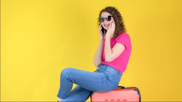 Atrakcyjna Młoda Dziewczyna Okularach Przeciwsłonecznych Siedzi Walizce Używa Smartfona Odizolowanego — Wideo stockowe