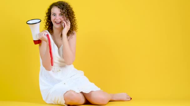 白いドレスの少女が黄色の背景にメガホンを手に電話で話す スピーカーで発表する女性 — ストック動画
