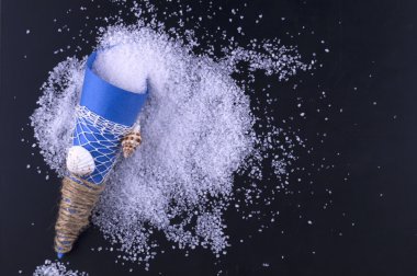 Sea salt in a blue paper bag is scattered on a black background. clipart