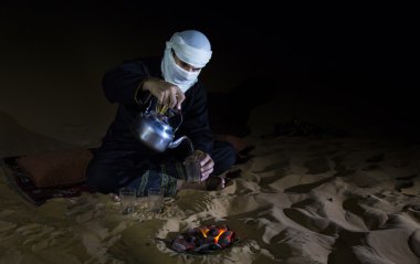 Man in traditional Tuareg outfit making tea in a desert clipart