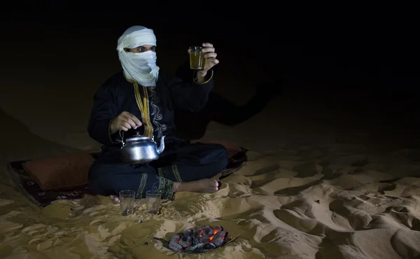 Mand i traditionel Tuareg outfit laver te i en ørken - Stock-foto