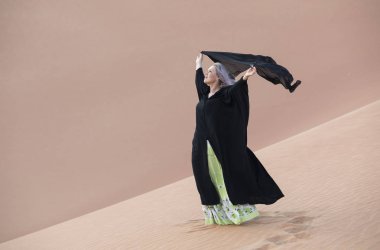 woman in abaya walking in a desert and holding flying shawl clipart