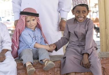 Nizwa, Umman, 10 Kasım 2017: omani çocuk ve Avrupa çocuk parapetin üzerinde otururken el sıkışan