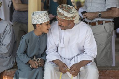 Nizwa, Oman, 10th November 2017: omani man touching rosary beads and talking with son clipart