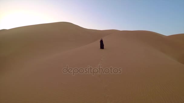 Femme arabe en hijab noir marchant dans le désert  