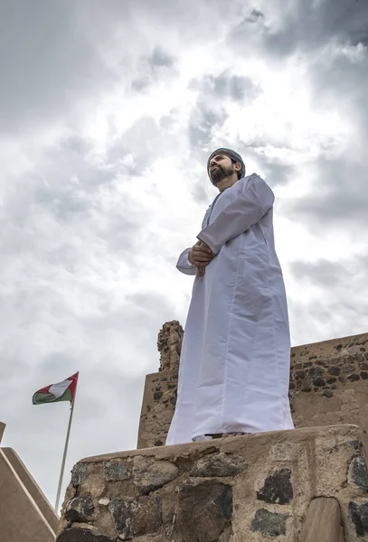 城の壁の背景にフラグ近くに立っている伝統的なオマーンの服でアラブ人 — ストック写真