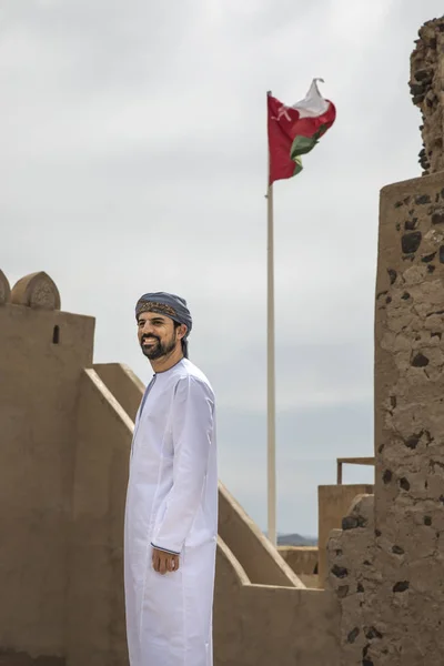 城の壁の背景にフラグ近くに立っている伝統的なオマーンの服でアラブ人 — ストック写真