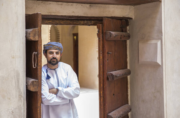 Closeup view of arab man wearing traditional omani outfit standing near opened wooden doors.