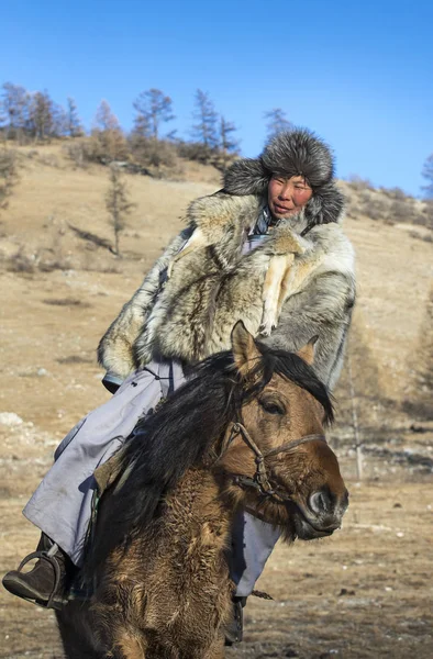 mongolian man wearing a wolf skin jacket, riding his horse in a