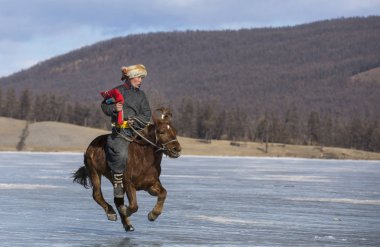 Hatgal, Mongolia, 1st March 2018: mongolian man riding a horse on a frozen lake Khovsgol clipart