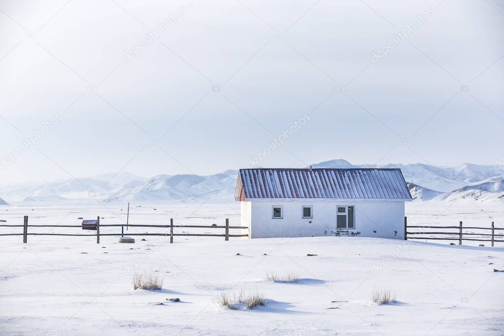 small white house in a snow covered valley in the middle of mountains of Northern Mongolia