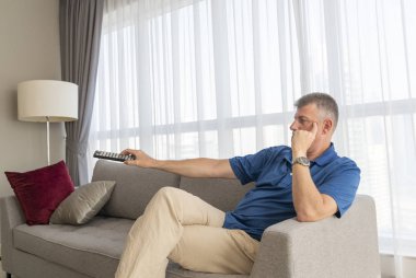 Orta yaşlı bir adam kanepede oturup televizyon izliyor.