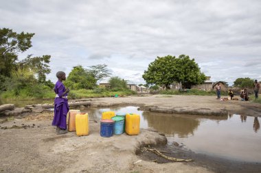 Aynı şekilde, Tanzanya, 11 Haziran 2019: Çamurlu deredeki maasai kızı içme suyu toplamak için.