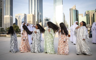 Abu Dabi, Birleşik Arap Emirlikleri, 14 Aralık 2019: Erkekler dans ederken saçlarını atan ve arka planda şarkı söyleyen kadınlar