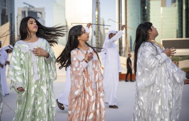 Abu Dabi, Birleşik Arap Emirlikleri, 14 Aralık 2019: Erkekler dans ederken saçlarını atan ve arka planda şarkı söyleyen kadınlar