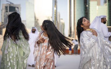 Abu Dabi, Birleşik Arap Emirlikleri, 14 Aralık 2019: Erkekler dans ederken saçlarını atan ve arka planda şarkı söyleyen kadınlar
