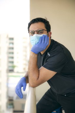 Tıbbi maskeli olgun bir adamın portresi balkonunda, kendini izole etme ve karantina konseptinde