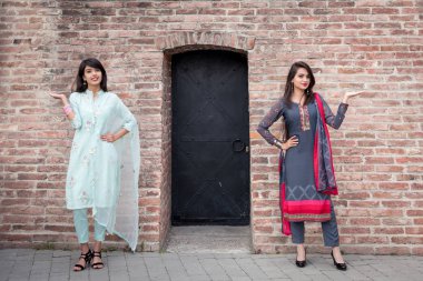 Two Indian girls in traditional dress stand at the entrance to the house. clipart