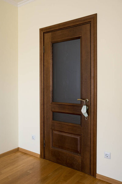 The door is closed and a white medical protective mask hangs on the door handle