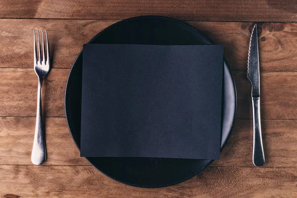 木製のテーブルの上に黒いプレートと刃物で構成されたランチ招待状. — ストック写真
