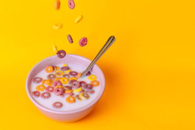 Süt ve kaşıkla pembe bir kaseye düşen renkli tahıllar..