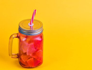 Kırmızı cam sürahi ve soğuk doğal içecek. Meyve parçaları ve sarı arka plan..