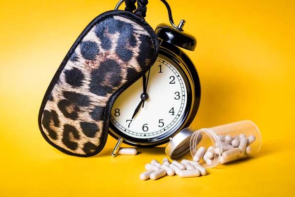 Insomnia concept. Alarm clock, leopard sleep mask and sleeping pills with yellow background.