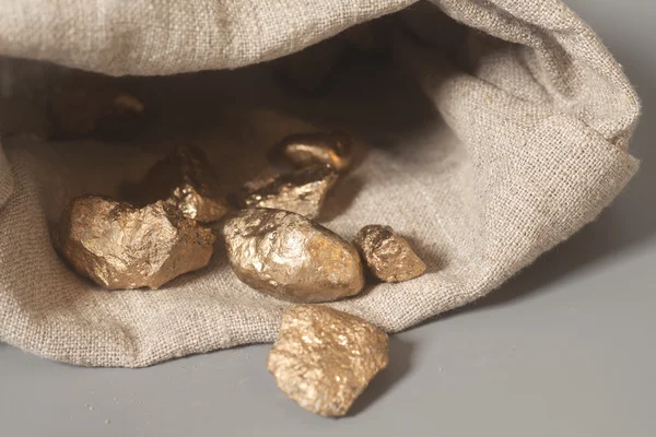 Altın nuggets çantası gri arka plan üzerinde üzerinden dışarı dökülmesini — Stok fotoğraf