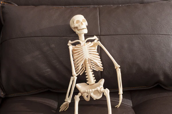 Esqueleto sentado en el sofá de cuero —  Fotos de Stock
