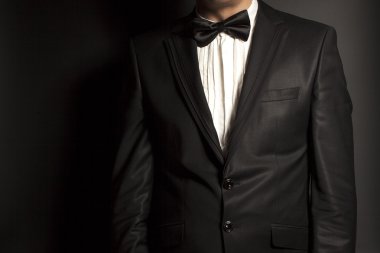 Siyah arka plan üzerine siyah takım elbise ve kravat giyen adam