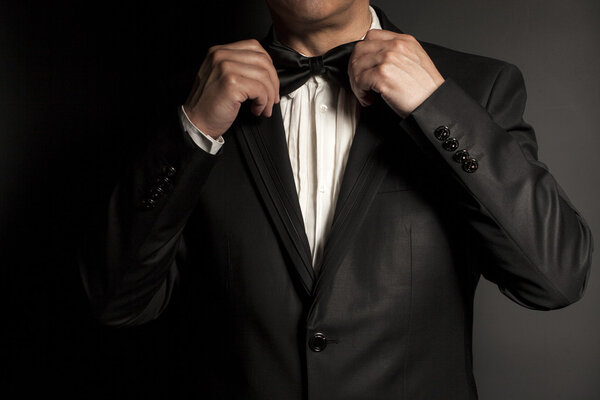 Close-up of  gentleman wearing black tie straightens his bowtie.