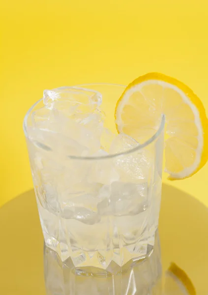 Beber con hielo y rodaja de limón sobre fondo amarillo — Foto de Stock