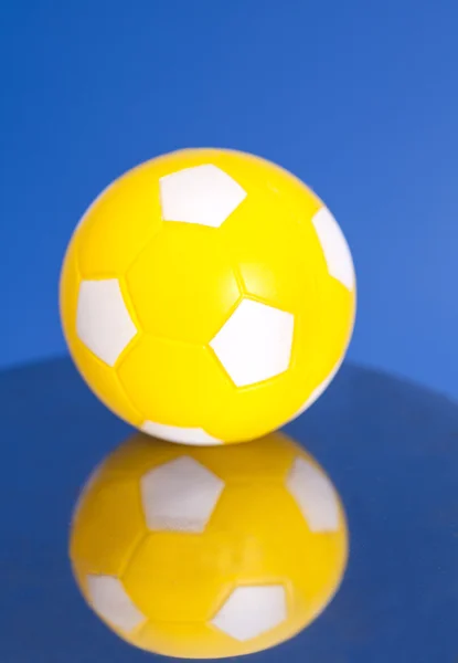 Gele voetbal met reflectie op blauwe achtergrond — Stockfoto