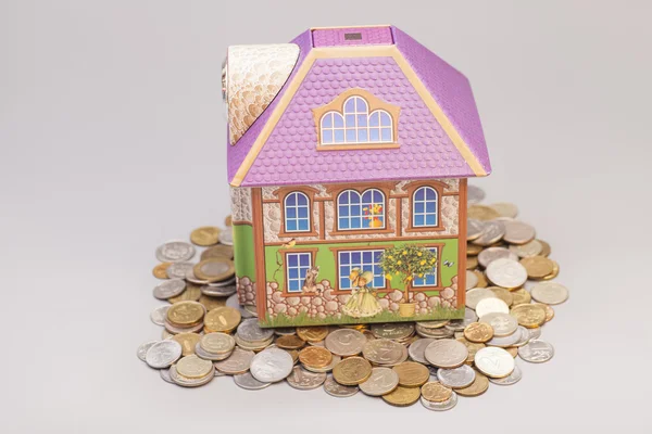 Dom stojący na sterty monet na szaro. Pojęcie nieruchomości — Zdjęcie stockowe